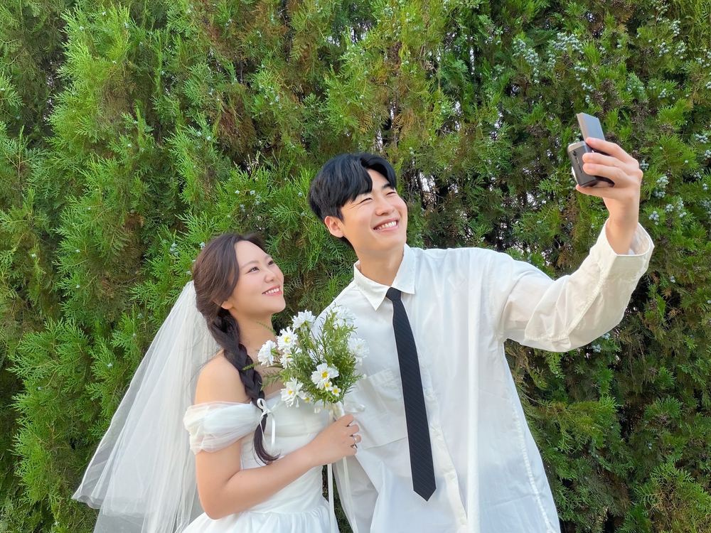 초록 나무 앞에서 함께 셀카를 찍는 두 사람